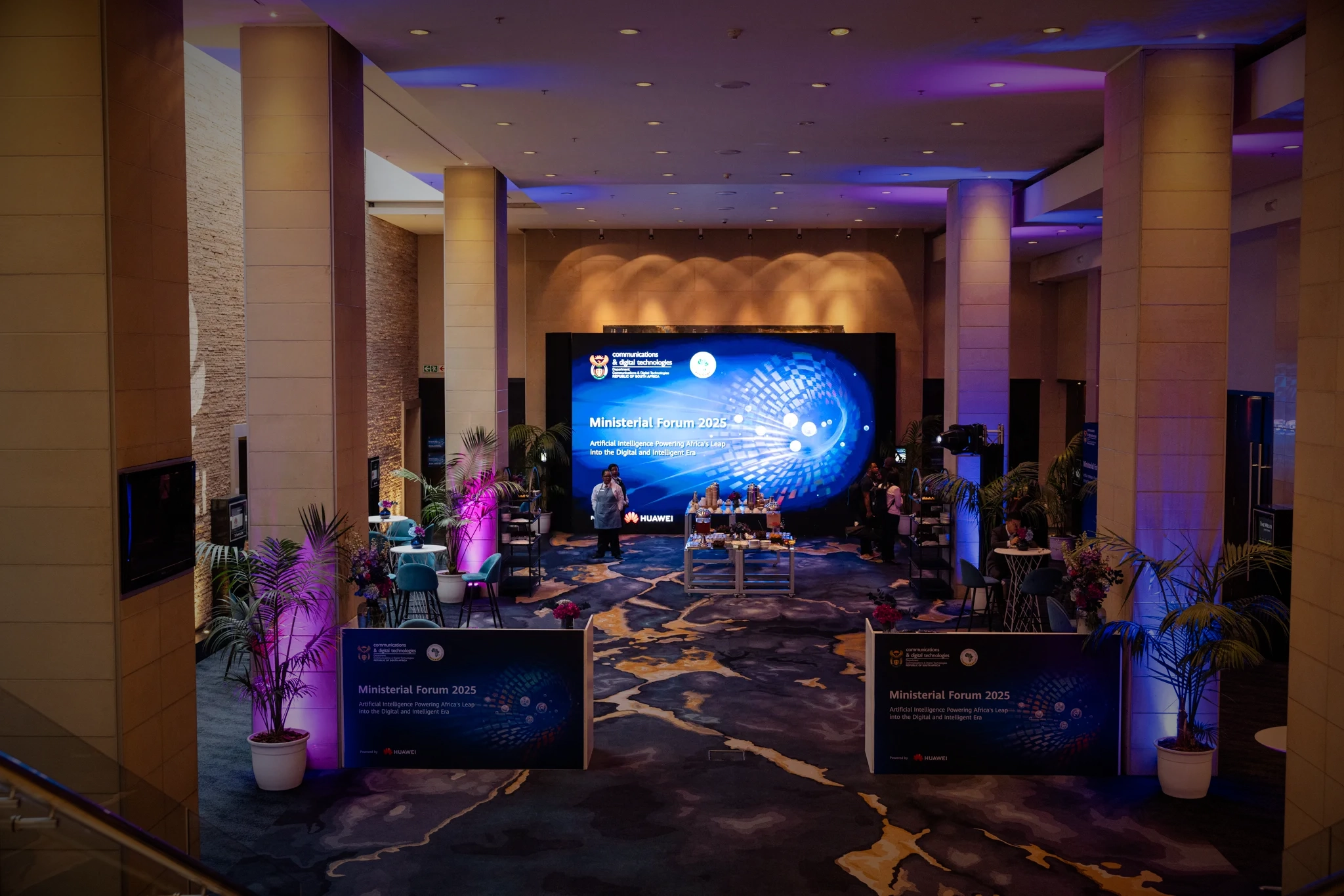 A lobby styled for the Ministerial Forum 2025 with an LED screen and purple uplighting